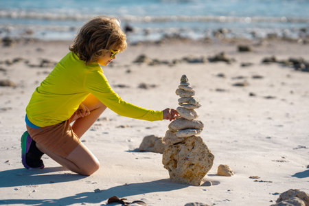 Little child playing with stones on the beach. Child play with pyramid of stones on the beach, sea seascape, rest and seaside kids summer vacation. Child playing on the beach and building stone tower.の写真素材