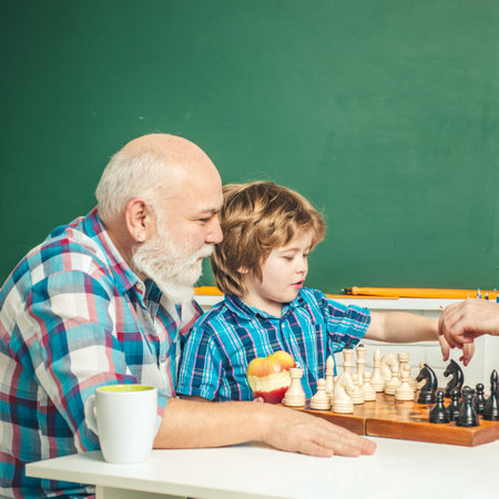 Grandfather and grandson playing chess. Grandpa teaching grangson at chess school.の写真素材