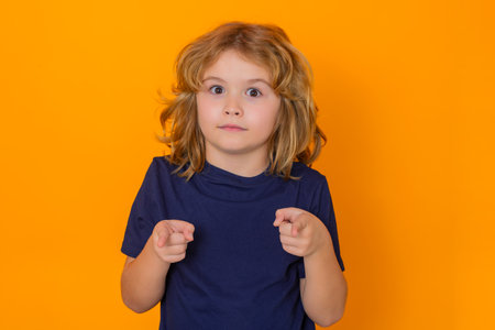 Child boy pointing you on yellow isolated studio background. Shocked kid with index finger pointing you with copyspace, showing promo offers, points.の写真素材