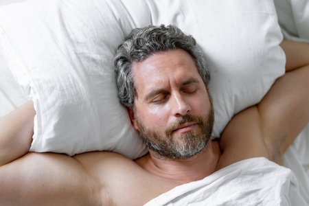Male sleeps on pillow. Gray hair man sleep in white bed. Senior man sleep in bed at bedroom. Mature man morning sleeps at home. Good sleep. Millennial man sleeping in bed. Morning bedtime rest sleep.の写真素材