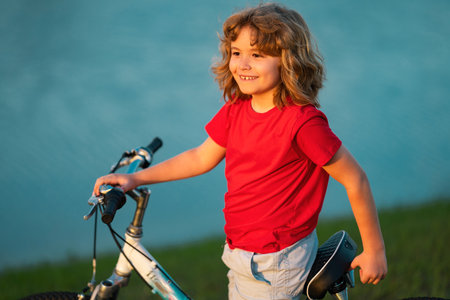 Happy kid boy riding bike in summer park. Bike dream. Dreamy kids face. Daydreamer child portrait close up. Dreams and imagination.の写真素材