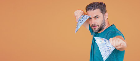 Handsome man holding money isolated over beige studio, banner. Money in dollar banknotes. Pile of...