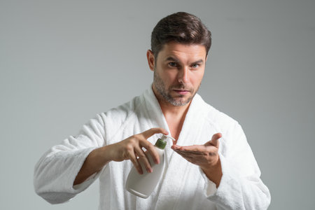 Organic cosmetics for man. Beauty man presentation beauty care product, bottle with dispenser pump for liquid soap, gel or foam. Natural man holding bottle cosmetic bottle on gray studio.の写真素材