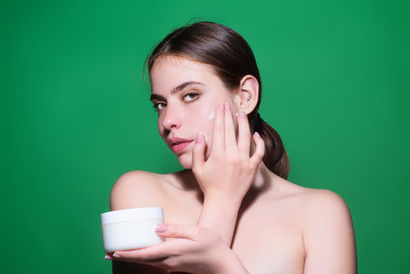 Woman putting cosmetic cream. Spa model applying skincare product on her face. Morning make-up. Moisturizing skincare cream, lotion or mask for skin lifting and anti-aging effect.の写真素材