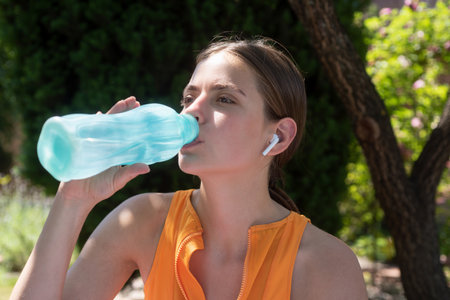 Fitness sport woman drinking water from bottle outdoor. Thirsty woman holding bottle drinks water....