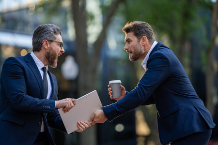 Businessmen fighting outdoor. Business conflict between business men in formal-wear in office. Office employee with aggressive expression fight. Angry office workers in city. Disagreed men partners.の写真素材