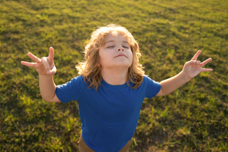 Child is meditating on green grass in the park with eyes closed on sunny summer day. Concept of meditation, dreaming, wellbeing and healthy kids lifestyle.の写真素材