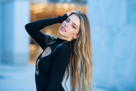 Beautiful sensual woman with long blonde hair. Sexy model in the street. High fashion model in black dress outdoor. Pretty woman outdoor portrait.の写真素材