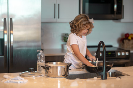 Kid washing dishes in the kitchen interior. Child helping his parents with housework. Kid boy washing dishes in the kitchen interior. Child helping his parents with housework.の写真素材