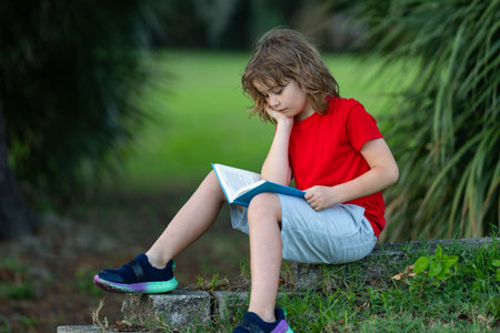 Cute kid reading book on meadow outdoors. School and education. Nature and park. Early learning. Little boy reading a book in summer park. Concept of childrens recreation without gadgets.の写真素材