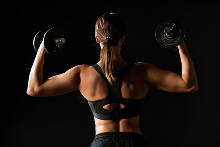 Strong woman with dumbbells. Slim girl holds dumbbells. Workout for sexy body. Fitness sexy woman with dumbbells on a dark background. Back view. Back of fitness woman. Slim woman with dumbbells.の写真素材