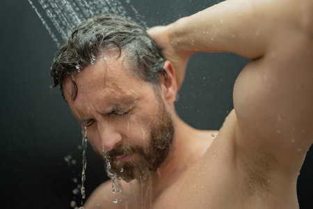 Middle aged man washing hair in bath. Guy bathing shower head in bathtub. Face in foam in shower. Bathing man taking shower. Closeup guy showering. Shower concept. Man is under water drops in showers.の写真素材