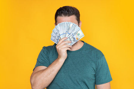 Good payment. Handsome man holding money isolated over grey studio. Money in dollar banknotes. Pile...