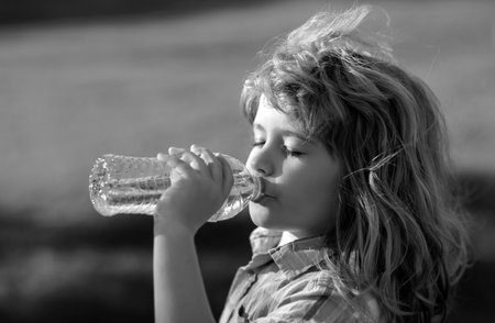 Close up portrait of kid drinking water from pet bottle outdoor.の写真素材