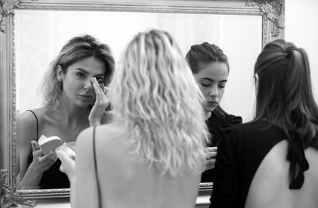 Women girlfriends applying make-up preparing for party, looking in mirror. Fashion and beauty woman, makeup, cosmetics.の写真素材