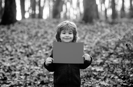 Autumn child holds a blank sheet for text space. Advertising and sale. Child holding advertising board, empty paper sheet. Seasons sale. Discount. Black friday. Marketing. Banner copy space for text.の写真素材