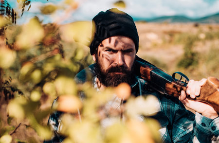 Bearded hunter man holding gun and walking in forest. Hunter with shotgun gun on hunt. Close up Portrait of hamdsome Hunter.の写真素材