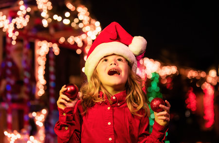 Happy little kid looks at the sky in the Christmas night. Happy kids portrait, Child enjoying winter holiday in the front yard. House Decorated with Garlands.の写真素材