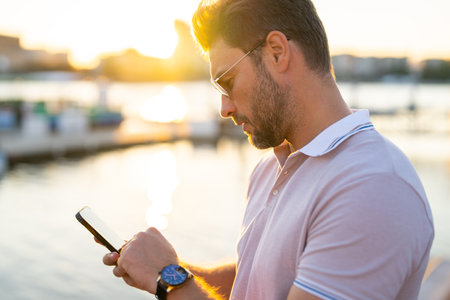 Young handsome man in classik polo t-shirt chatting on phone on the street. Handsome confident stylish hipster model talking on phone outside. Business phone conversation.の写真素材