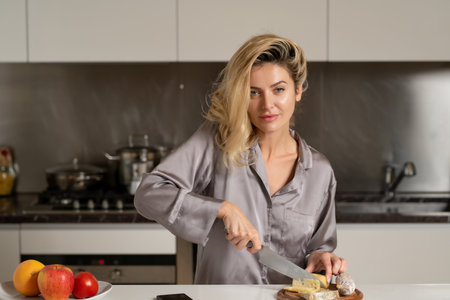 Sexy woman preparing food, cutting cheese and sausage in the kitchen. Woman wearing sexy pajama cooking breakfast in home kitchen.の写真素材