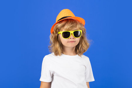 Fashion portrait of child boy in summer hat, t-shirt and sunglasses on blue studio isolated...