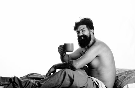 Good morning. Man in bed hold coffee ot tea cup. Young man is lying on bed and enjoying the morning.の写真素材