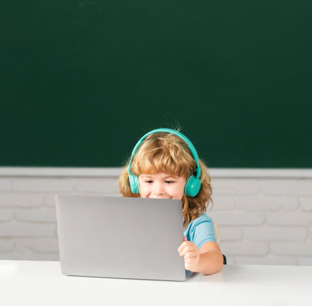 Small boy in headphones watch video lesson on computer in school, child in earphones have online lesson, using laptop. Elementary school and education.の写真素材