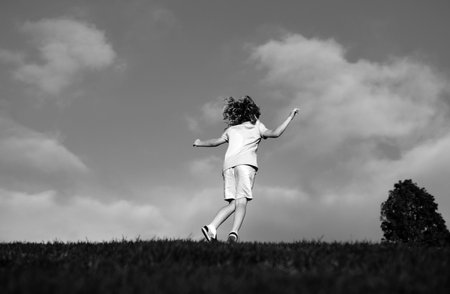 Child boy running on meadow. Back view of kid run on beautiful summer field.の写真素材
