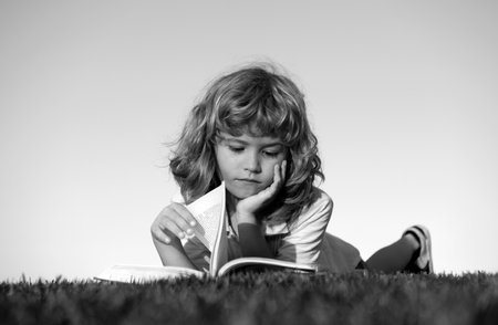 Smart kid boy reading book in park outdoors.の写真素材