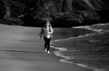 Kids playing on beach. Children play at sea on summer family vacation. Sand and water fun, sun protection. Little athlete in training. Runner exercising, jogging for kids.の写真素材