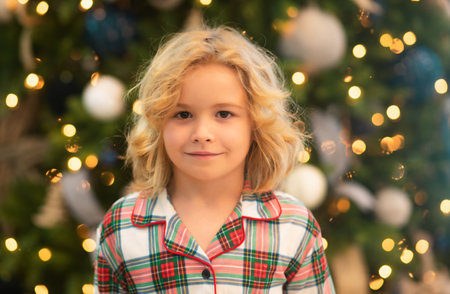 Happy funny child in winter pajama near Christmas tree at morning. Christmas and New Year concept.の写真素材