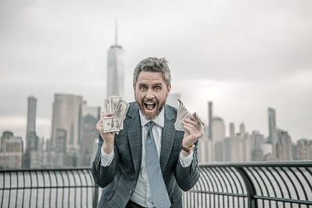 Businessman with dollar outdoor. Businessman excited with dollar money on street. Businessman in suit hold dollar cash. Mature man in suit hold 100 dollars banknotes at city. 100 dollars banknote.の写真素材