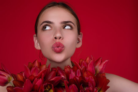Valentines Day. Beauty girl with tulip. Beautiful sensual woman hold tulips bouquet, studio portrait on red background. Close up beauty woman face near tulips bouquet.の写真素材