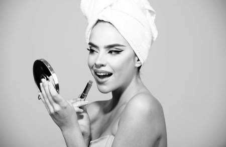 Portrait of a beautiful young girl with bright make-up. Woman with towel on head applies red lipstick, painting lips of young beauty model girl.の写真素材