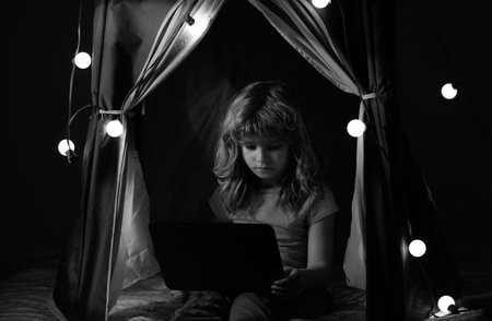 Child sitting in home tent playing with laptop. Social media for kids.の写真素材