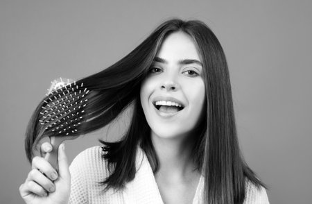 Amazed woman combing hair. Close up portrait of female model with a comb brushing hair. Girl with hairbrush, hair care and beauty. Closeup female face.の写真素材