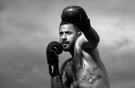 Muscular kick boxer or muay thai fighter punching. Kickboxing fighter in boxing gloves hitting shadow, training for competition. Boxing training outside.の写真素材