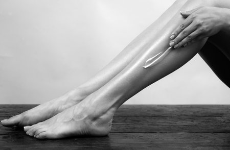 Young woman applying body lotion on legs. Cosmetic cream on woman leg with clean soft skin. Applying moisturizer cream on legs. Cellulite or anti cellulite treatment. Body care and spa salon concept.の写真素材