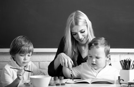 Portrait of schoolkids and teacher talking at school lesson. Happy family. Mother and two son together draw, paint. Mom helps the children boys.の写真素材