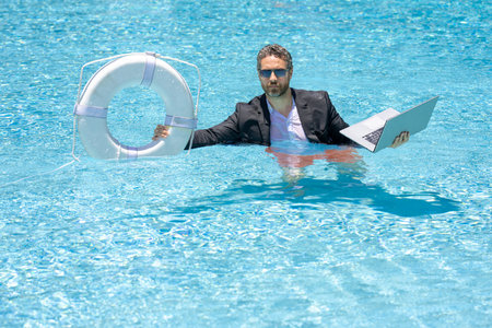 Rescue business. Business man in suit hold laptop and rescue lifebuoy in swim pool. Rescue swimming ring for businessman. Rescue businessman. Save and help business.の写真素材