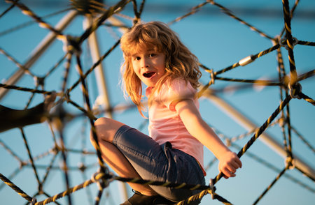 Child climbing the net. Child boy climbed on top of the rope web on playground. Kids play and climb...