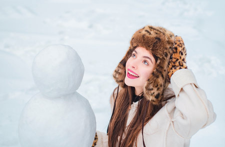 Joyful Beauty young woman Having Fun with snowman in Winter Park. Funny snowmen. Happy smiling girl make snowman on sunny winter day.の写真素材