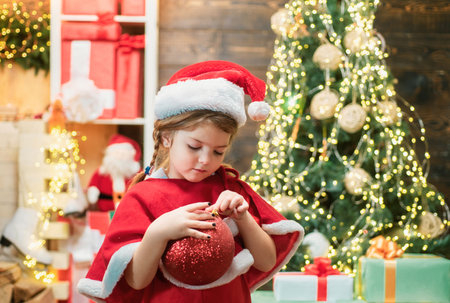 Christmas kid decorating Christmas tree with bauble. Little girl in Christmas dress decorating Christmas tree with baubles.の写真素材