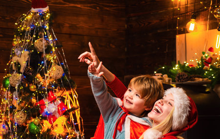 Happy new year. Childhood moments. Gifts for winter holidays at fire place. Christmas interior. Elf child. Portrait of happy mother and adorable baby celebrate Christmas.の写真素材