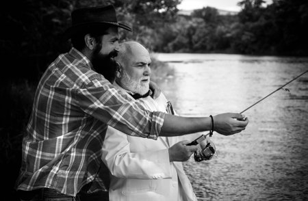 Fly rod and reel with a brown trout from a stream. Father and son relaxing together. Men fishing in river during summer day. Man fishing.の写真素材