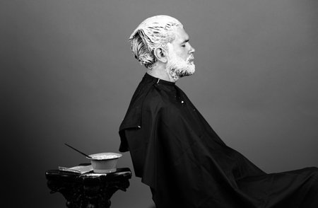 Barber shop. Portrait of bearded man color hair. Process of a man hair coloring at hairdresser salon.の写真素材