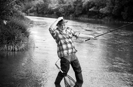 Excited senior man fisherman with fishing rod, spinning reel on river. Old man catching fish, pulling rod while fishing on lake.の写真素材