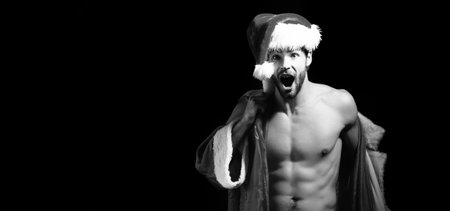 Christmas sexy man. Excited men in santa hat. New year strip and gifts for adults. Muscle amazed man at xmas. Santa with muscular body. Sexy santa claus guy on black background.の写真素材