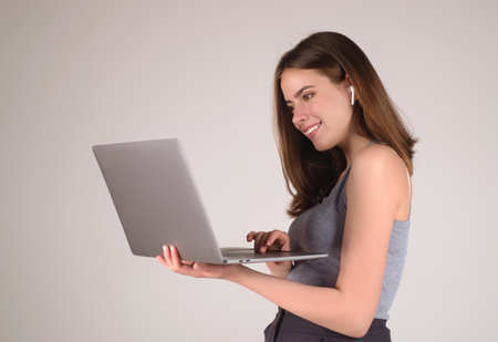 Happy Student. Woman Student in white t-shirt holding laptop and laptop, isolated over gray background. Student posing in studio. Portrait of student having video-call. Students time.の写真素材