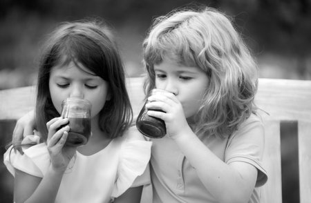 Brother and sister drink smoothie, kids summer cocktail in spring park outdoors. Little boy and girl kids enjoying spring. Kids walking at backyard. Best friends two children.の写真素材